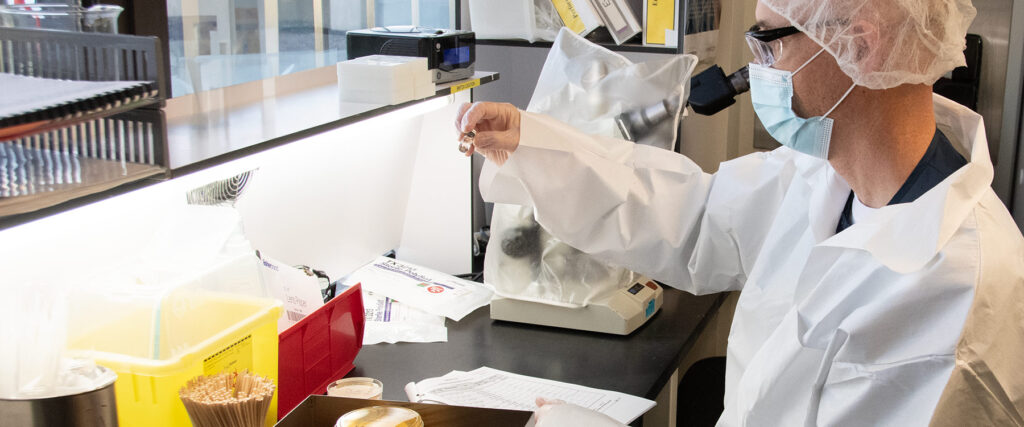 A lab technician looks at a vial of fluid in a QC testing lab.